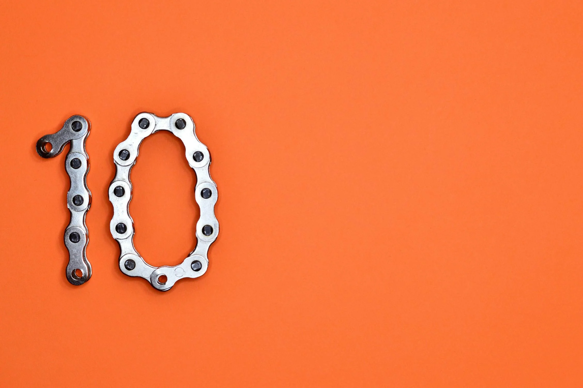 Number ten formed from a silver bike chain on an orange background, representing the Ten Essential Lending Tools to transform your business in 2025.