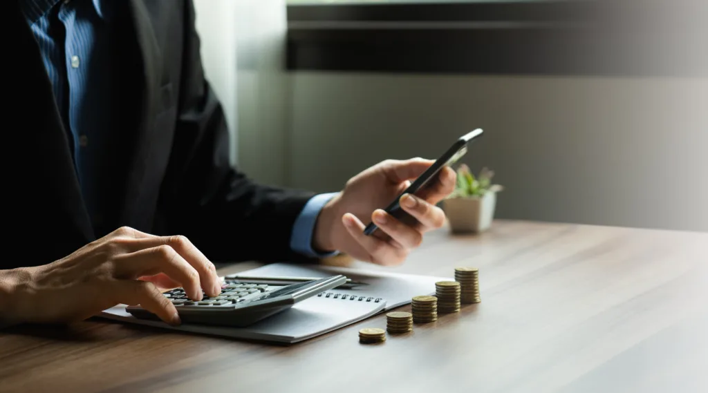 Person using a calculator beside stacked coins while reviewing credit costs.