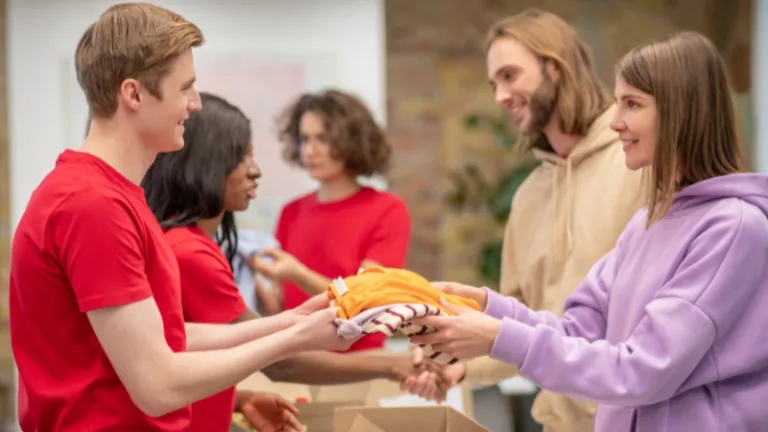 Volunteers handing folded clothes to people at a donation center.