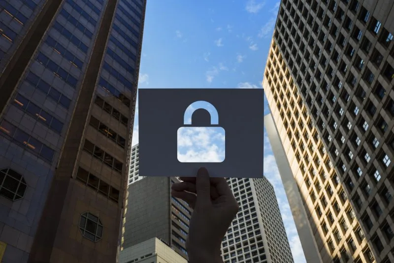 Person holding paper lock symbol against city skyscrapers, representing secure lockbox payment processing for lenders.