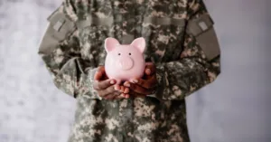 Servicemember in uniform holding piggy bank, symbolizing financial protections from SCRA military benefits.