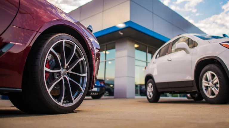 Vehicles parked outside an automotive dealership, representing auto financing and lending compliance.