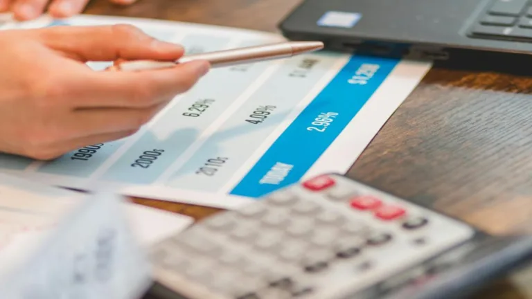 Hand pointing at an interest chart representing the rule of 78 beside a calculator.