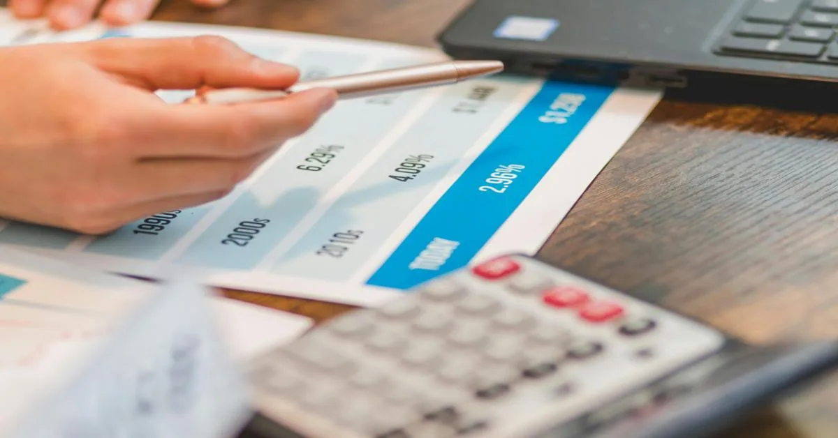 Hand pointing at an interest chart representing the rule of 78 beside a calculator.