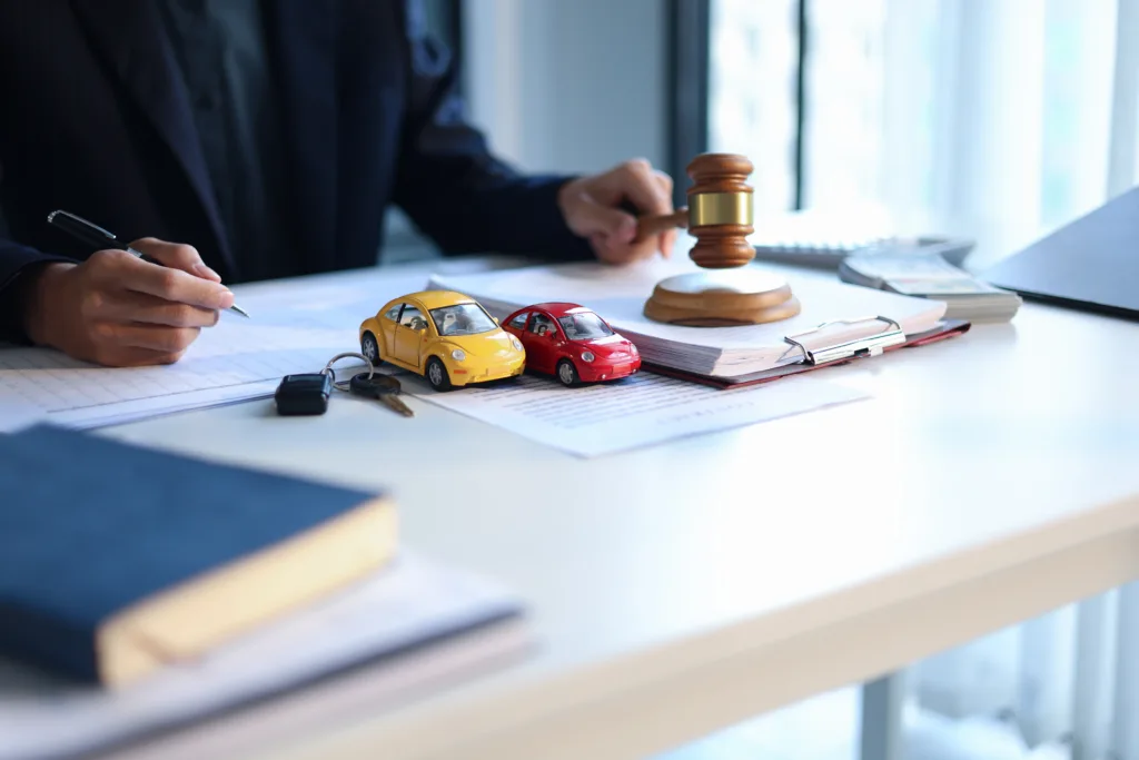 Auto loan documents with model cars, keys, and a judge’s gavel on a desk.