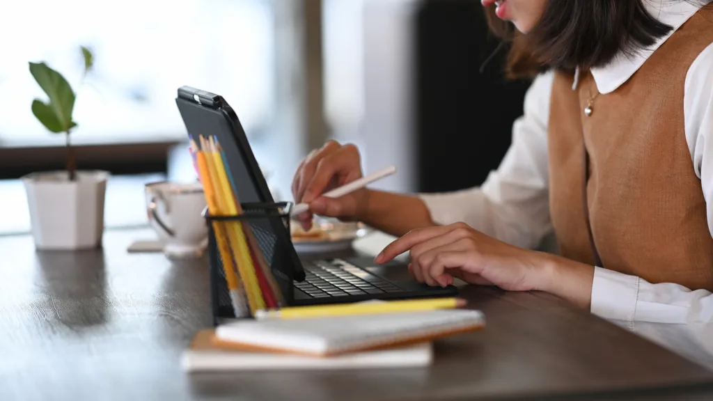 A person working at a desk using a tablet with a keyboard, stylus, and pencils.