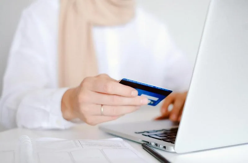 Person holding a credit card while using a laptop, representing Nortridge’s comprehensive payment solutions including credit, debit, ACH, and lockbox support.
