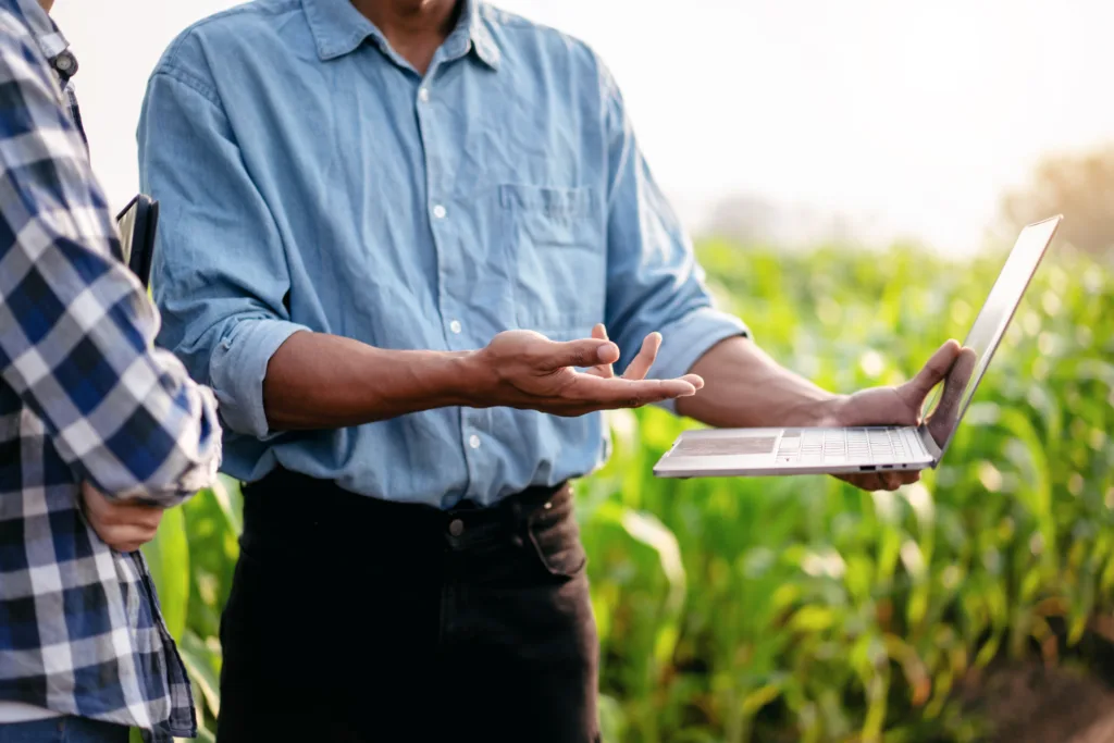 Two agriculture professionals discussing crop financing on a laptop in a field.