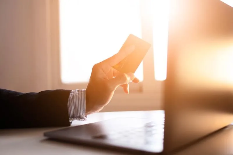 Businessperson using a laptop while holding a credit card in bright sunlight