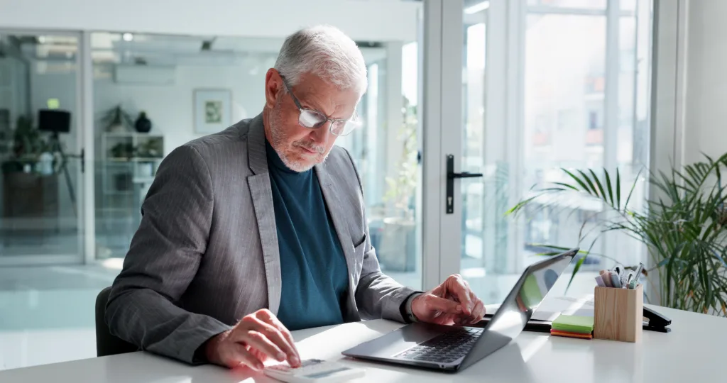 Man calculating loan costs while working on a laptop in an office.