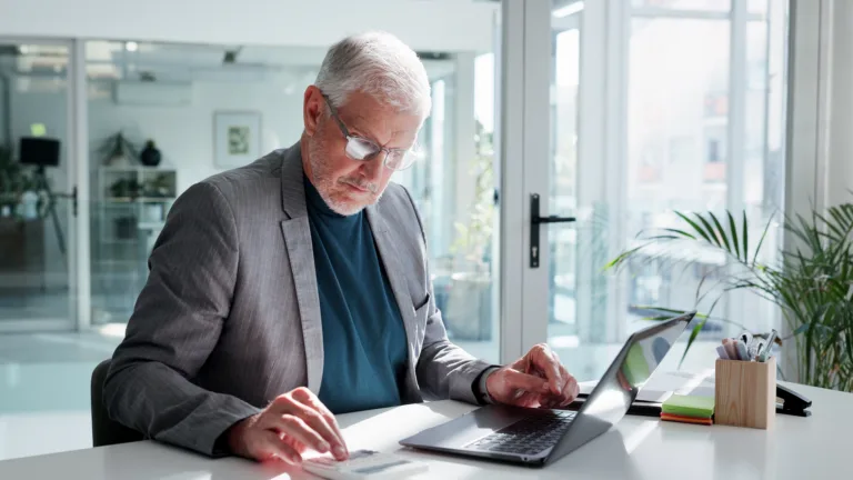 Man calculating loan costs while working on a laptop in an office.