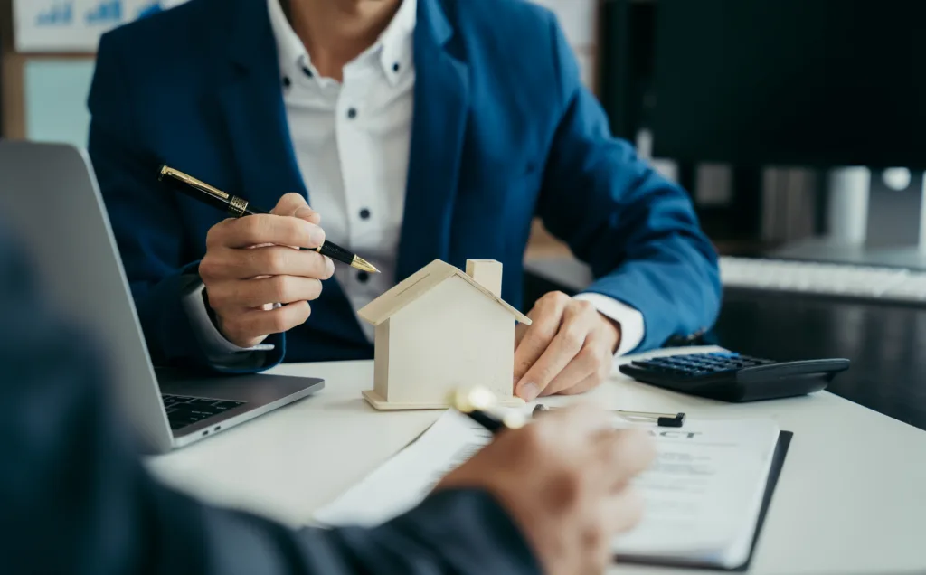 Financial professional explaining reverse mortgage terms with a home model and loan documents.