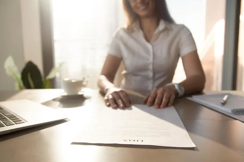 Woman reviews participation loan agreement terms at a sunlit desk.