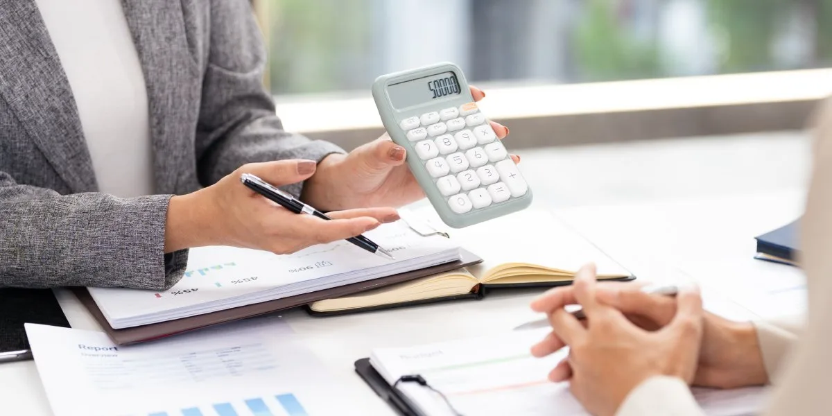 Loan servicer reviewing loan portfolio performance reports and budget figures with calculator