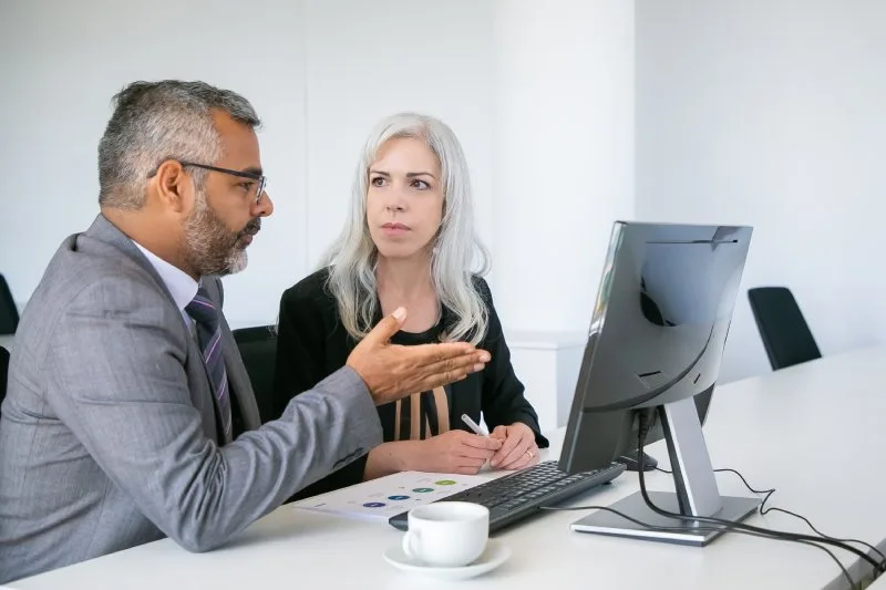 Loan servicing colleagues discussing operational efficiency and portfolio performance reports at a computer 