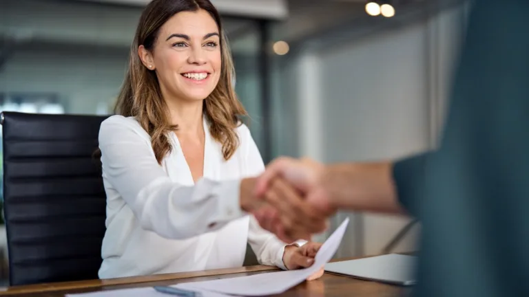 Loan servicing professional shaking hands with a borrower after signing loan paperwork.