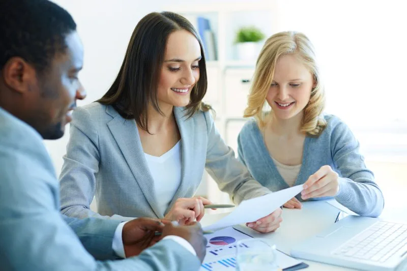Three loan servicing professionals reviewing portfolio performance reports together at office desk