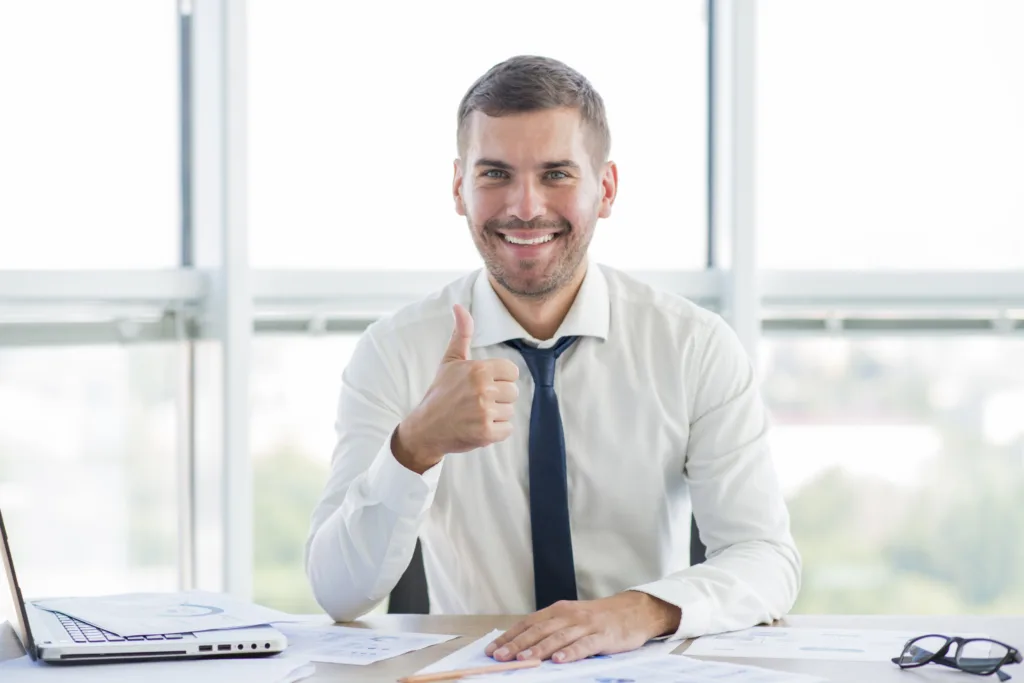 Loan servicer giving thumbs up at desk with laptop, confident in software choice 
