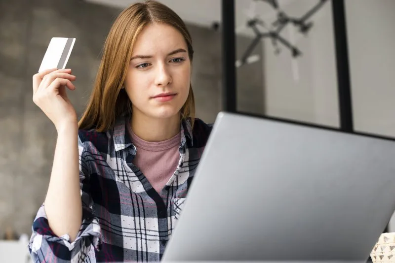 Young woman holding a credit card while using a laptop for online payment holiday application, and loan management