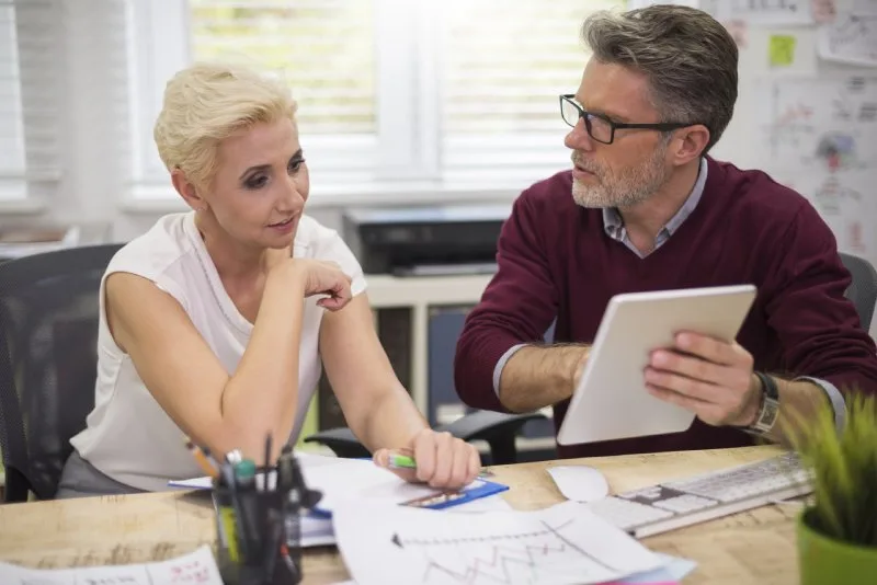 Woman and man reviewing paperwork with a rising and falling line chart at a desk. 