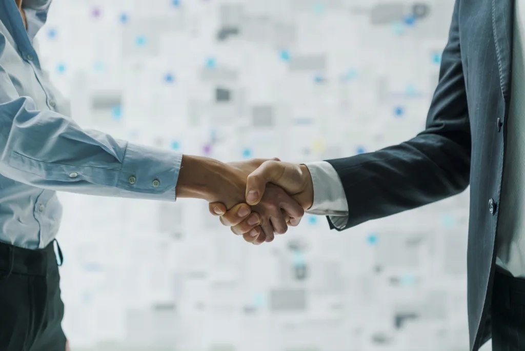 Two professionals in business attire shaking hands in front of a blurred digital background.
