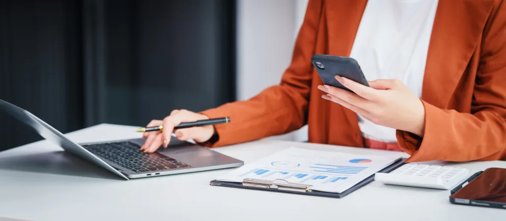 Business professional reviewing financial charts while using a laptop and phone.