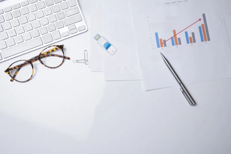 Loan portfolio performance charts and bar graphs printed on desk beside keyboard and glasses