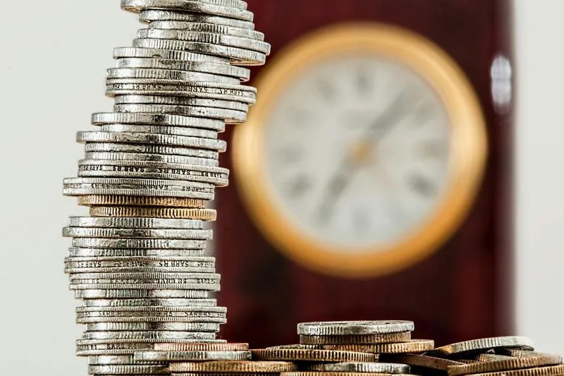Stack of coins in front of a blurred clock background.