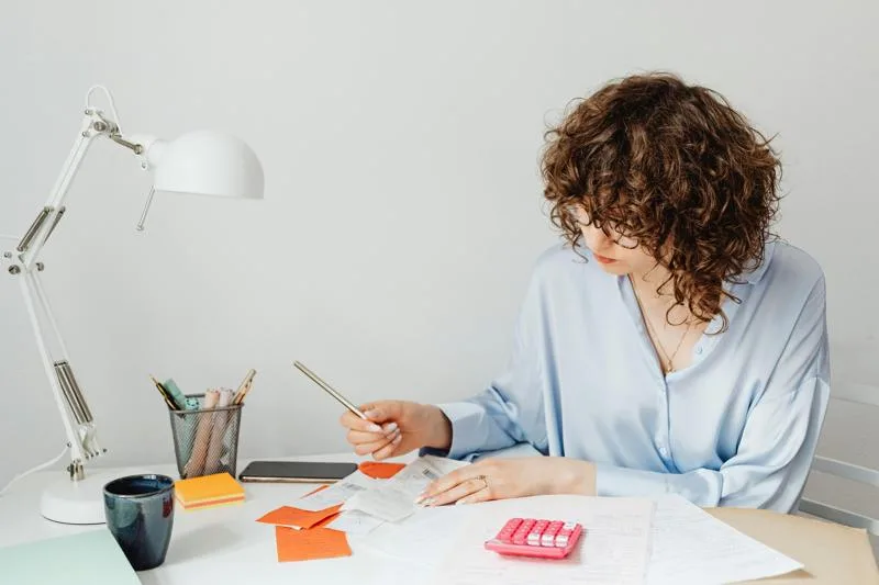 Woman calculating documents at desk with pen and receipts.