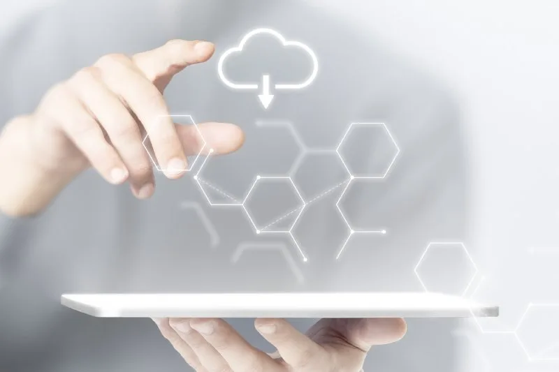 Hand reaching toward a glowing cloud icon and connected hexagon network graphics above a tablet. 