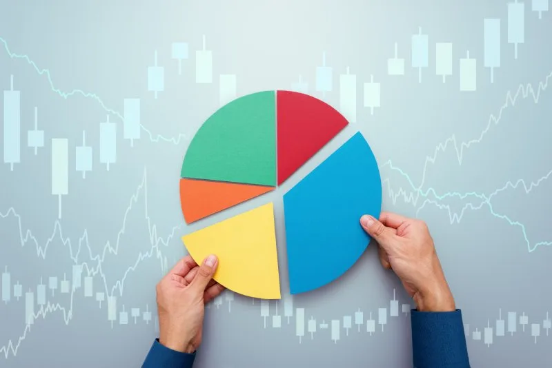 Hands holding colorful pie chart segments against a background of financial graphs and market trends.