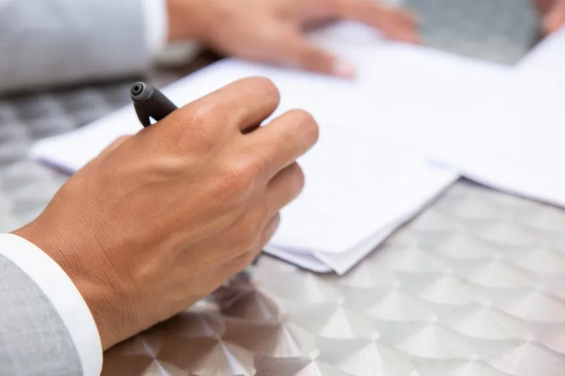 Close-up of professional hand signing loan agreement paperwork symbolizing borrower commitment in syndicated loan deals.