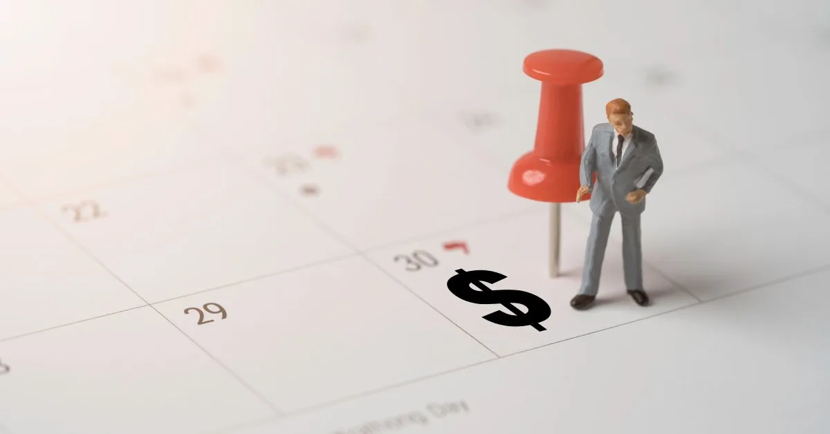 Businessman figurine standing on a calendar with a dollar sign representing payment holiday scheduling and loan management decisions