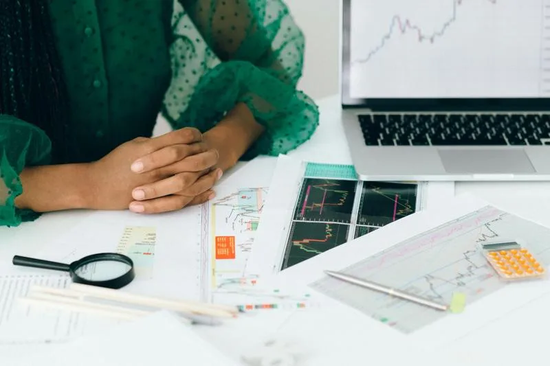 Hands folded near financial charts, magnifier, and laptop analyzing credit performance.