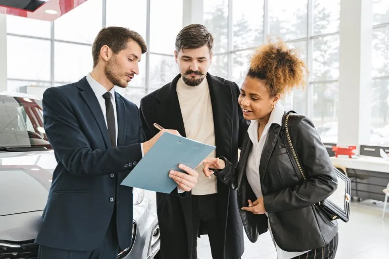 Auto dealer reviewing indirect auto financing terms with two borrowers at a dealership