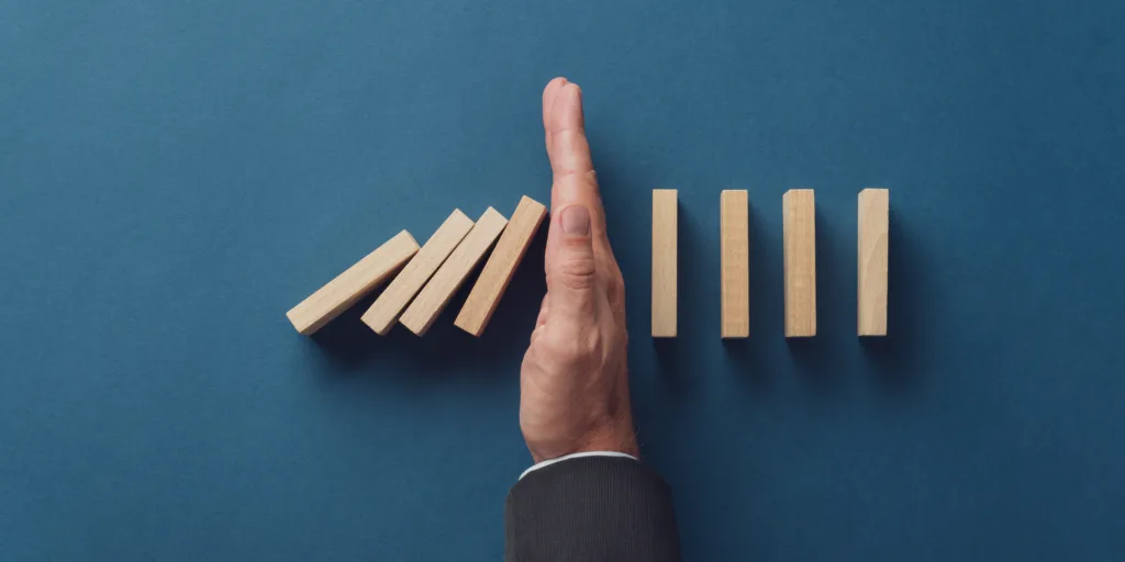 A businessman's hand stopping a row of falling wooden dominoes, symbolizing effective risk management.