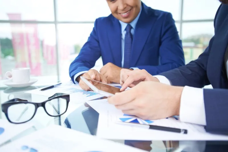 Two bankers reviewing loan portfolio performance charts and data on a tablet. 